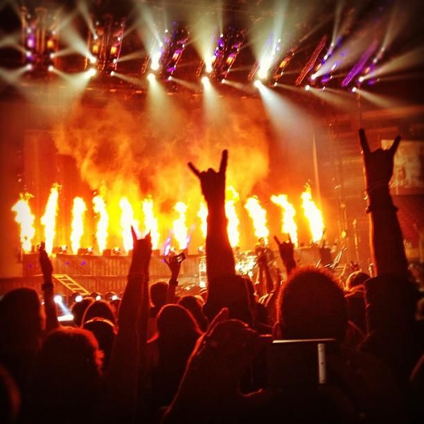 heavy metal crowd image facing the stage where pyro technics are shown and a silhoutte of a hand in is shown