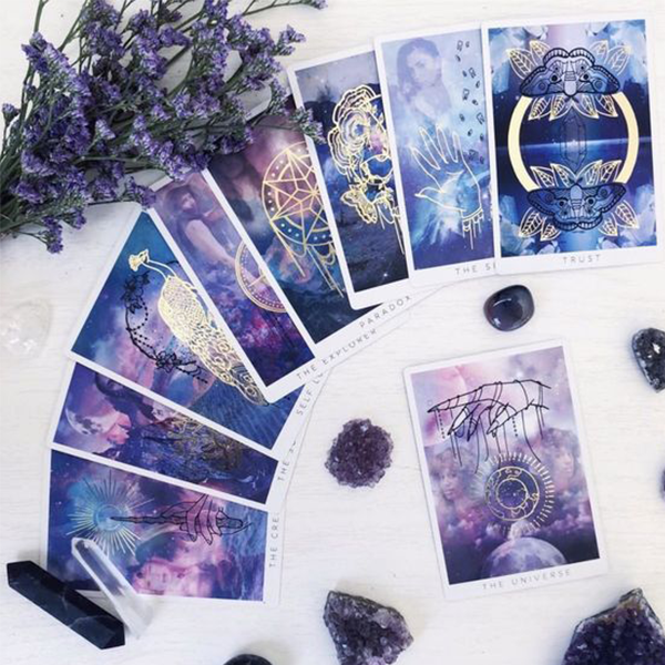 purple watercolor tarot cards on a white table surrounded by lavendar and different black and purple crystals